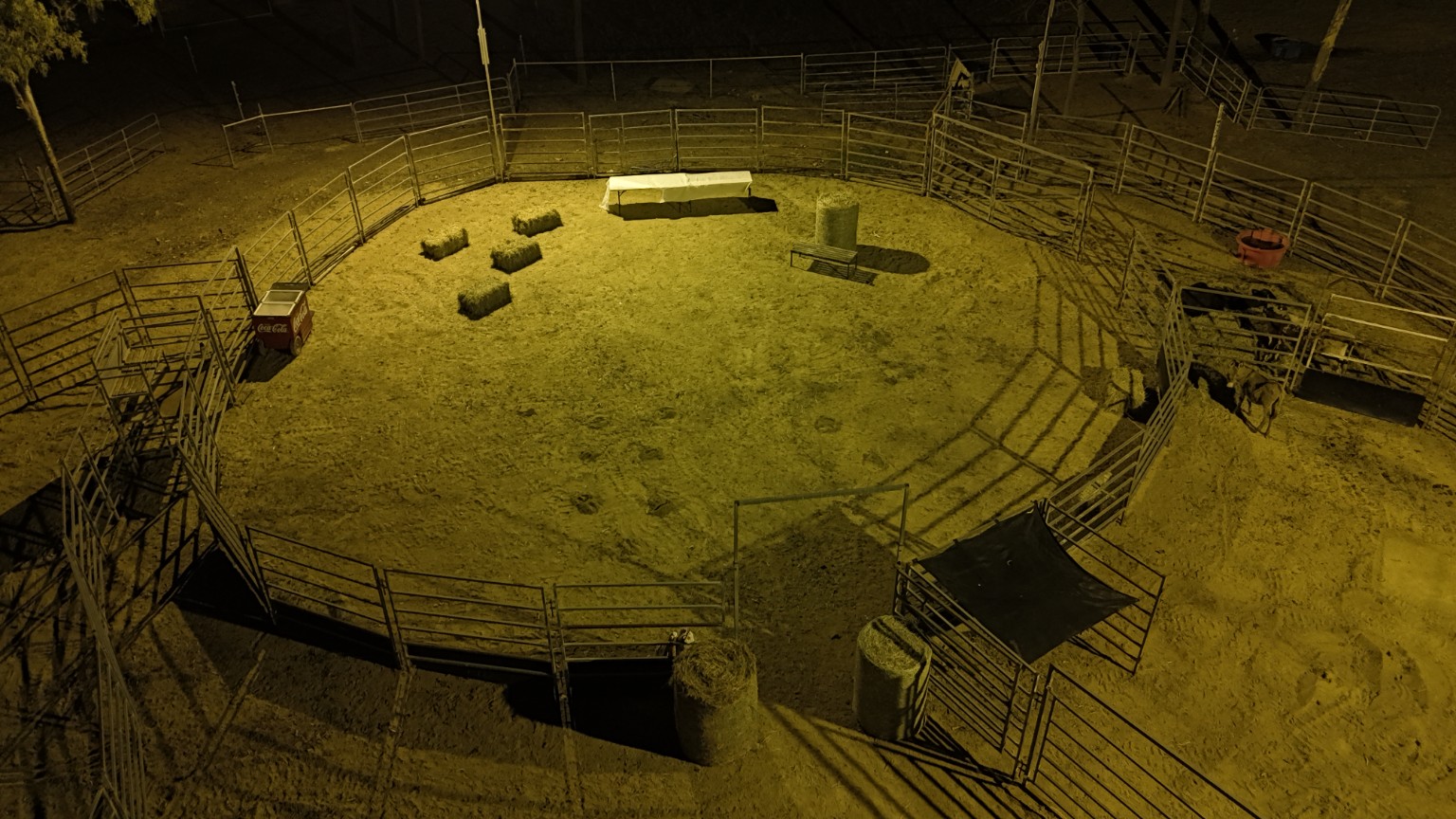 Actual aerial evening photograph of the roundyard under its existing lights, with hay bales and tables visible